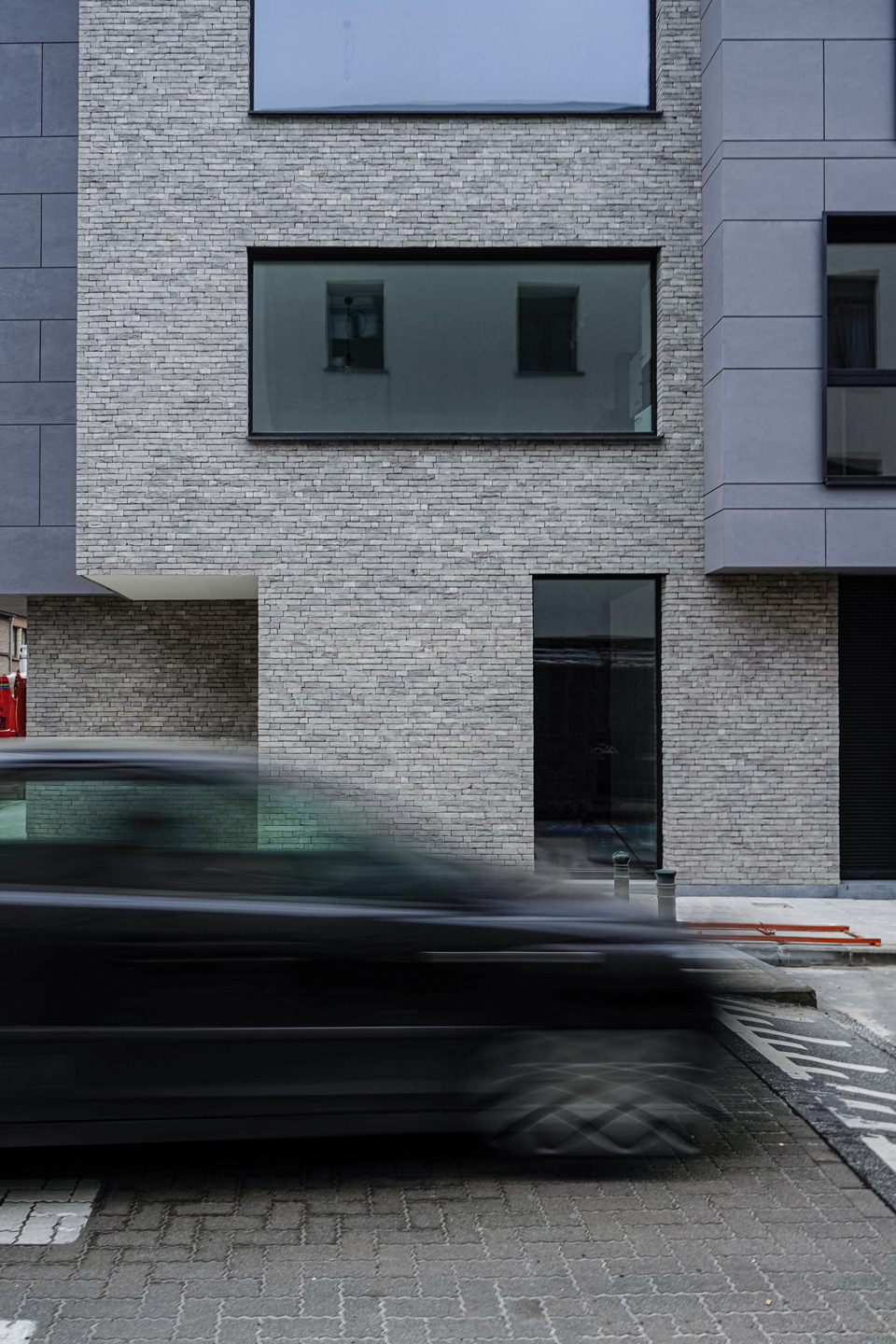 A corner building with a modern facade featuring grey bricks and fibre cement siding and large openings to enhance the 'eyes on the street' presence